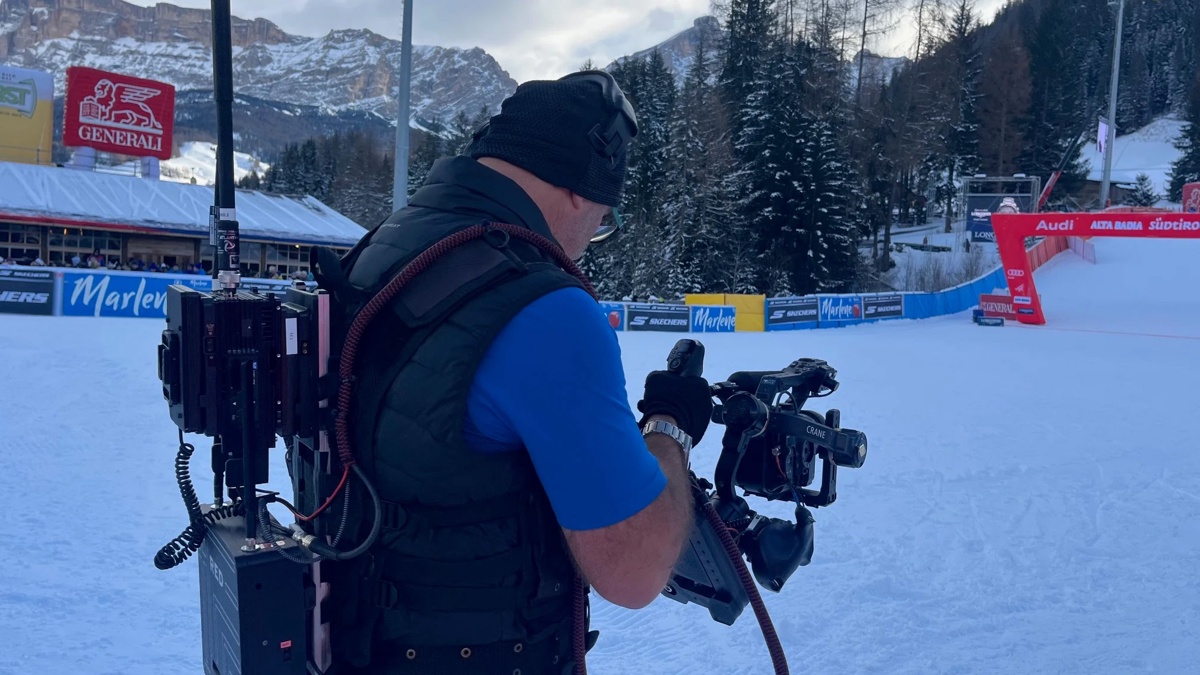 A camera operator with a wireless broadcast rig filming at the finish area of an Alpine ski World Cup race in the mountains
